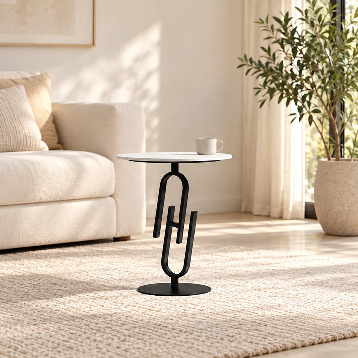 White round side table with black paperclip-shaped pedestal in a styled lounge with a cup and natural plant