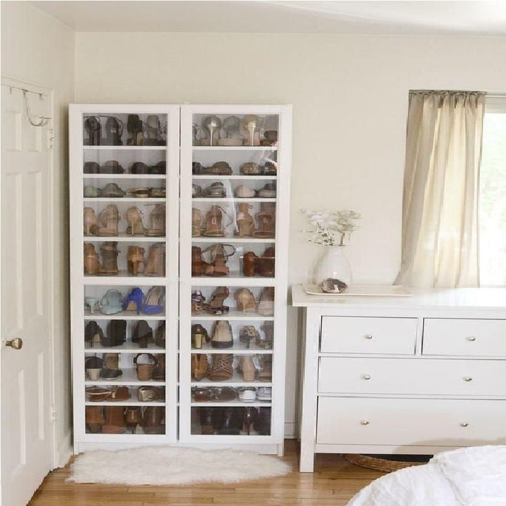 Tall white storage cabinet with glass doors filled with shoes beside dresser in bedroom