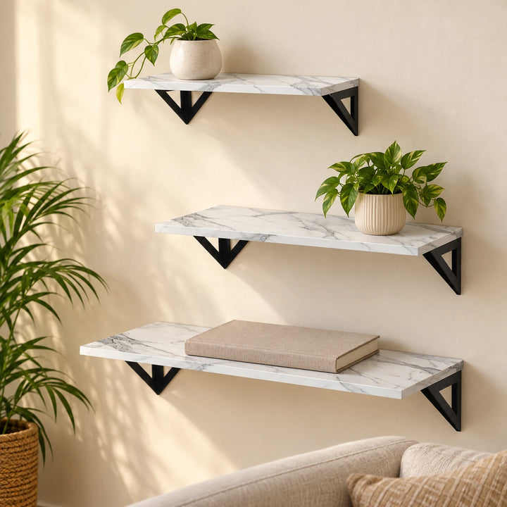 Set of three white marble-pattern floating shelves with black triangular brackets in a sunlit home