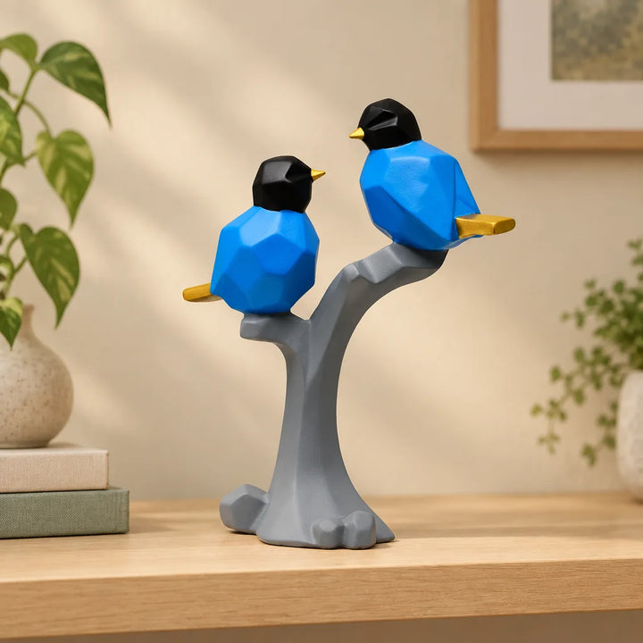 Two blue geometric bird figurines with black heads on grey branch, displayed on wooden shelf