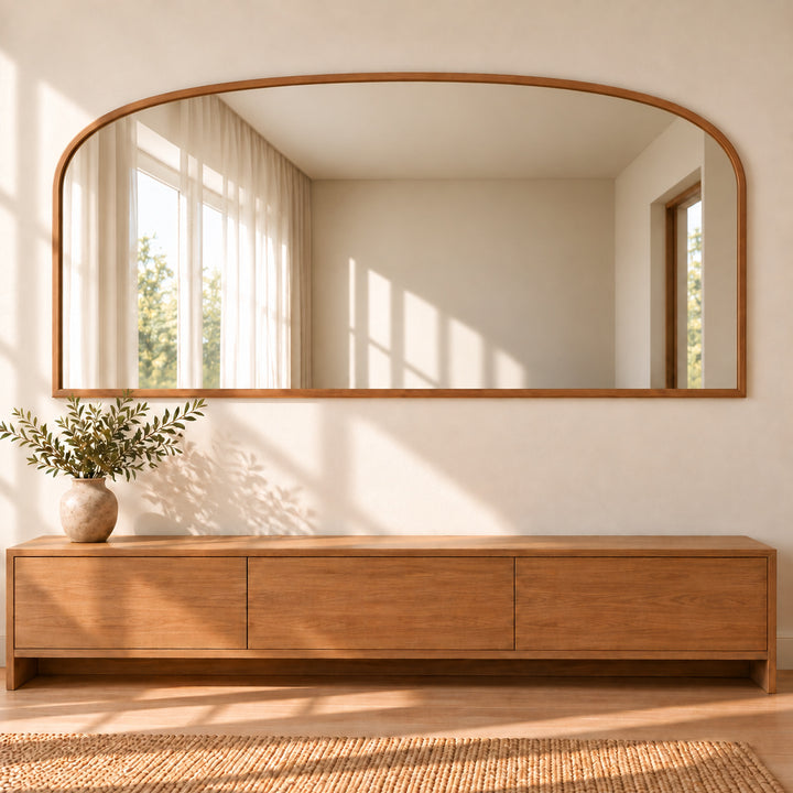 Wide horizontal arched mirror above a long wooden dining sideboard with greenery. Digitally styled visualization.
