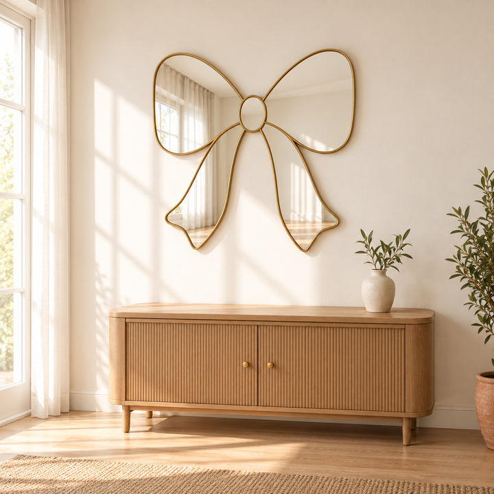 Bow ribbon wall mirror above a wooden sideboard with a small leafy vase. Digitally styled visualization.