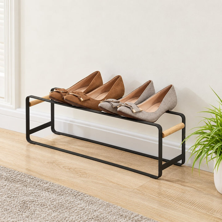 One Kiru black metal shoe rack unit with natural wood side handles and two pairs of shoes against a wall