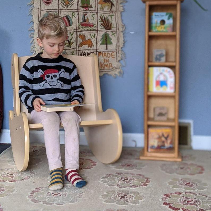 Child sitting on wooden whale rocker kids chair beside tall shelf