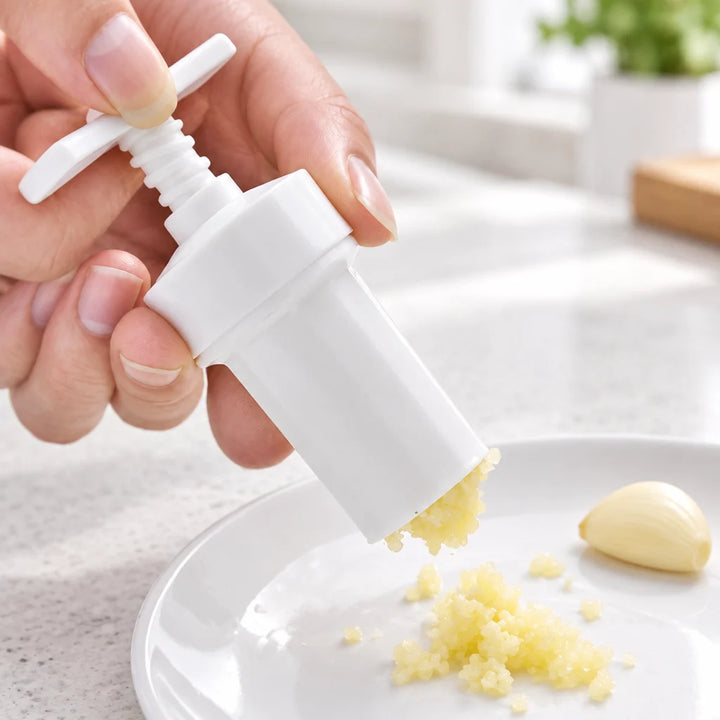 White handheld garlic masher pressing crushed garlic onto a plate