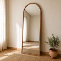 Arched full length standing mirror with a slim oak wood frame leaning against a cream wall