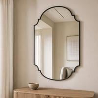 Shield shaped wall mirror with curved bracket corners and a black frame above a fluted console