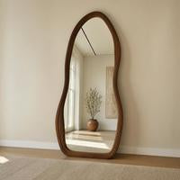 Asymmetrical wavy full length floor mirror with a walnut wood frame against a cream wall