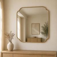 Square wall mirror with scalloped cut corners and a slim gold frame above a wooden console
