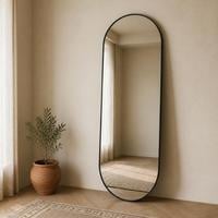 Capsule shaped full length mirror with a slim black metal frame leaning against a cream wall