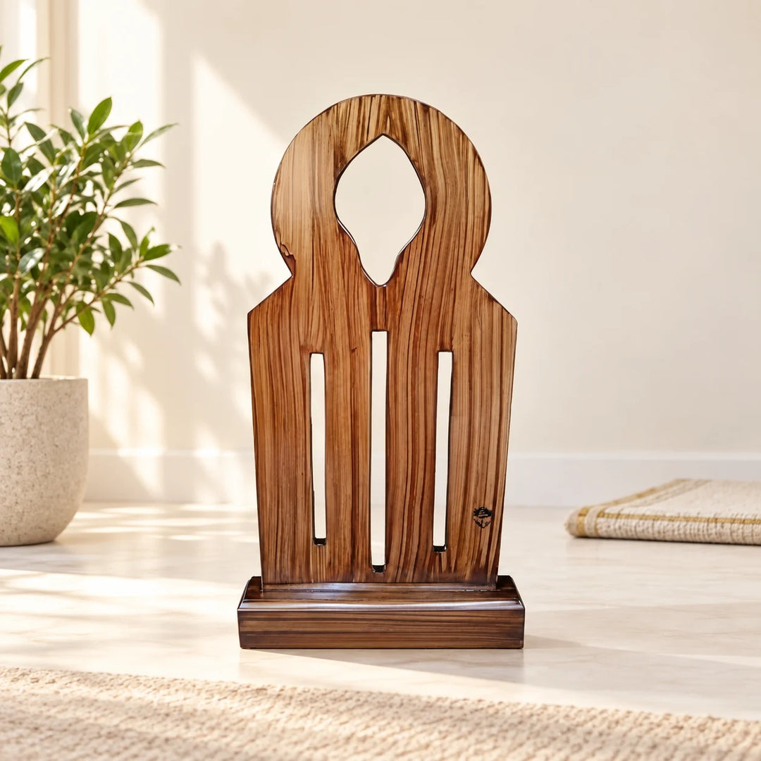 Wooden arched prayer sutrah with three vertical slots in a natural-light prayer corner beside a plant