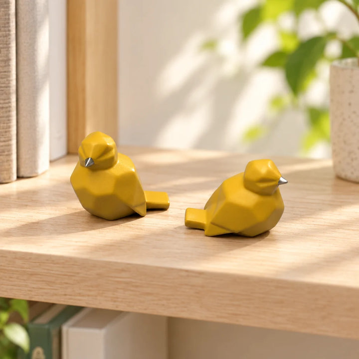 Pair of yellow geometric bird figurines on light wooden shelf in sunlit room