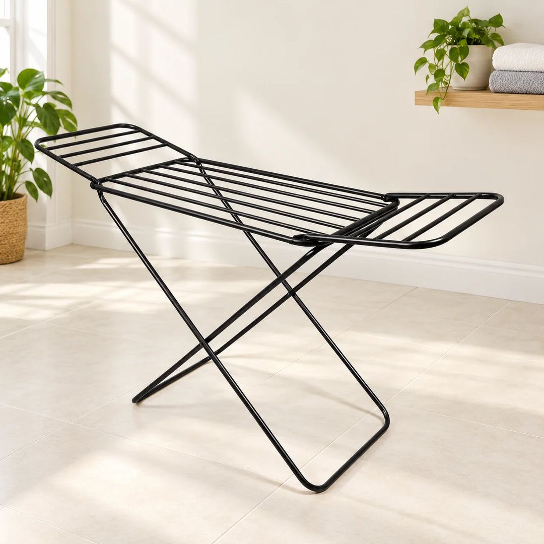 Black folding drying rack with raised wings in a bright laundry nook with a natural plant