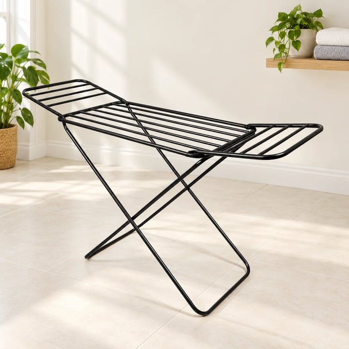 Black folding drying rack with raised wings in a bright laundry nook with a natural plant