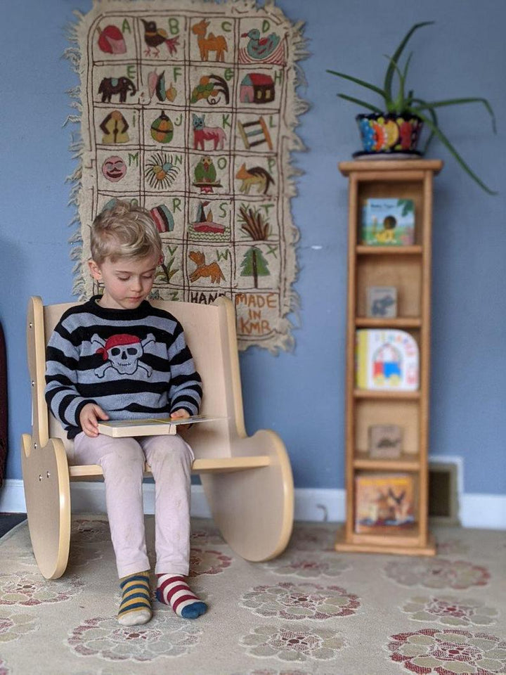 Child sitting on wooden whale rocker kids chair beside tall shelf