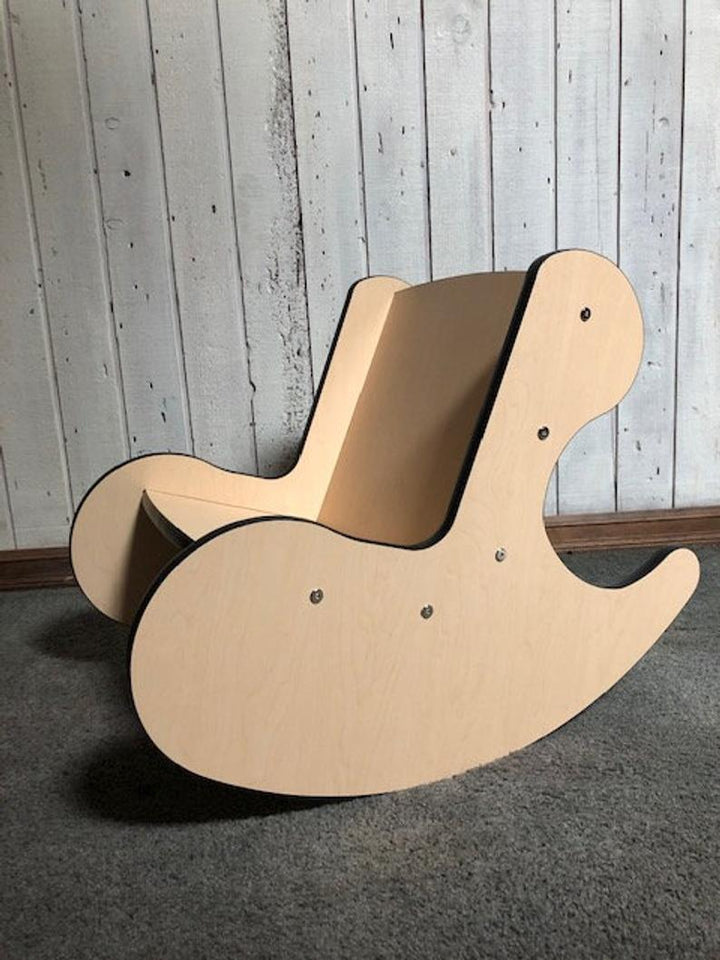 Plywood whale rocker kids chair on carpet against grey wood wall, side angle