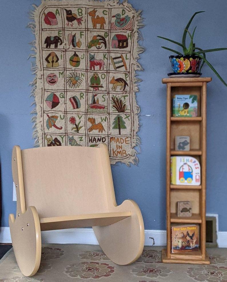 Wooden whale rocker kids chair in playroom next to narrow bookshelf
